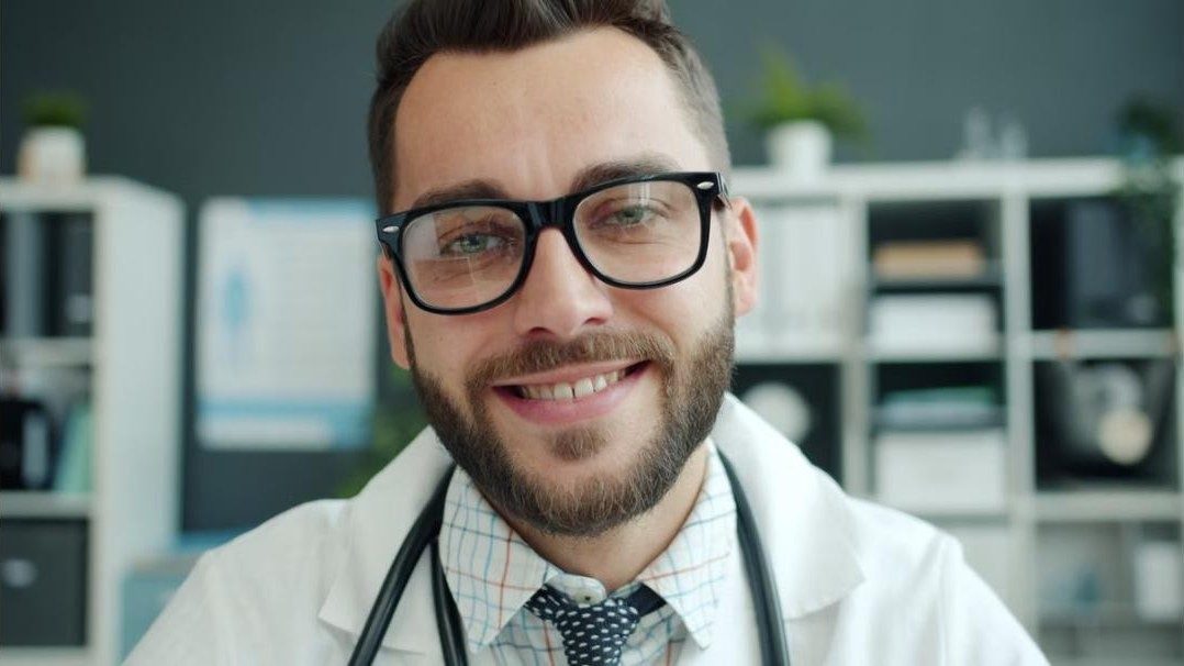 Lächelnder Arzt mit Brille in seiner Praxis. Nachweis am Bild: Foto: Vitaly Gariev / Pexels
